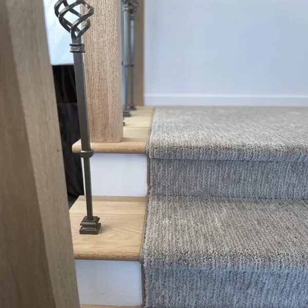 Close-up of light oak stairs, carpet, and iron spindle