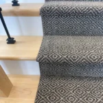 Detail of grey patterned runner on light wood stairs.
