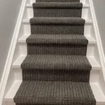 Full view of grey carpet runner on white and wood stairs