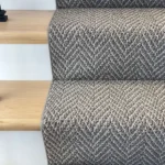 Gray herringbone carpet runner on light wood stairs