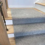 Grey carpet runner on light wood stairs, front view.