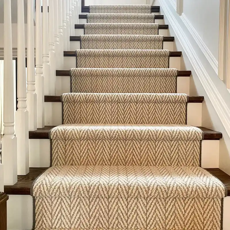 Neutral herringbone carpet runner on dark wood stairs