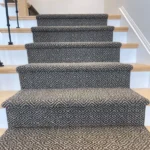 Patterned grey carpet runner on wooden stairs.